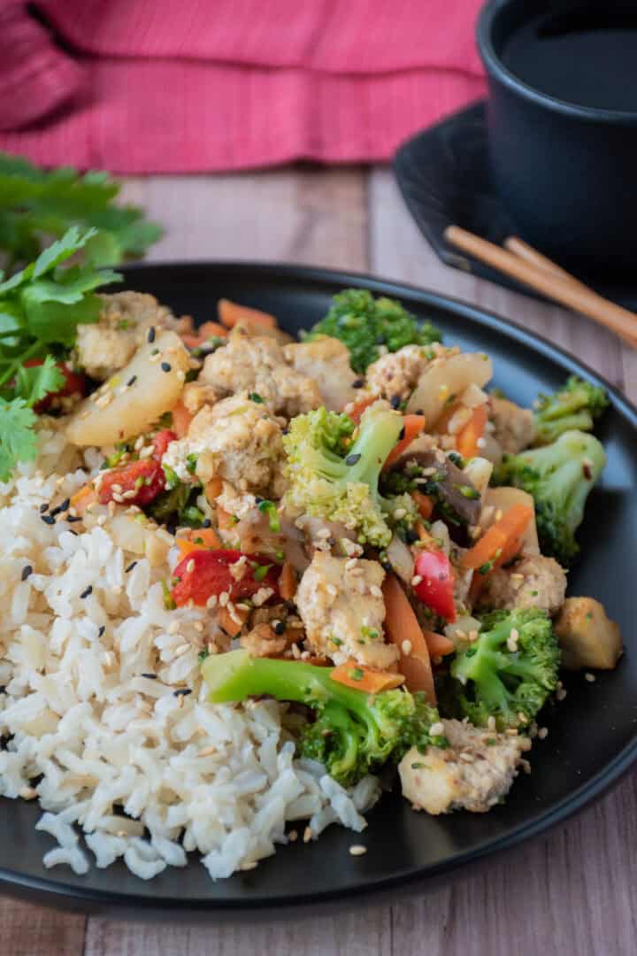 Stir fry on a plate, over brown rice, garnished with sesame seeds and cilantro.