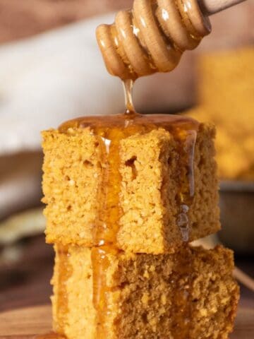 2 slices of cornbread stacked on one another, with honey being drizzled over them.