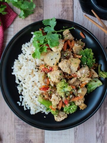 Stir fry on a plate, over brown rice, garnished with sesame seeds and cilantro.