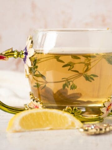 Tea in a glass mug, with thyme sprigs in it.