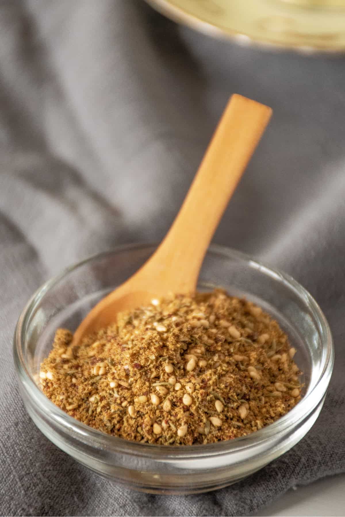 Small glass bowl with spice blend in it and a small wooden spoon.