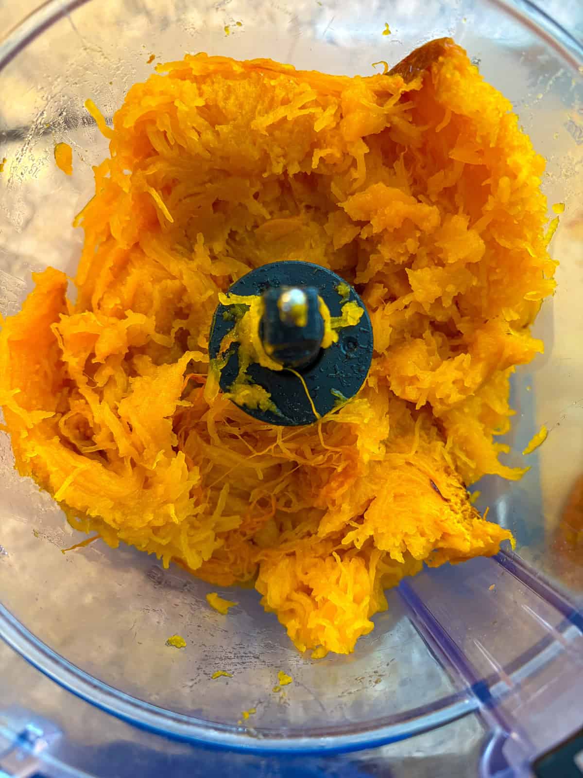 Baked flesh of a pumpkin scooped into the bowl of a food processor.