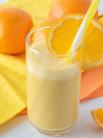 Orange drink in a glass with a straw, garnished with an orange slice.