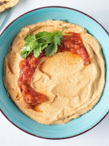Bowl of hummus, garnished with salsa and cilantro.
