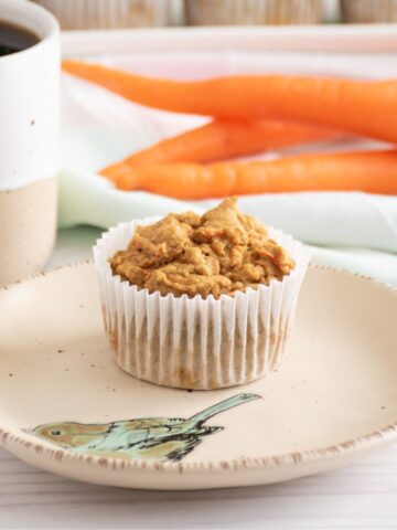 A muffin on a plate, with a cup of coffee nearby.