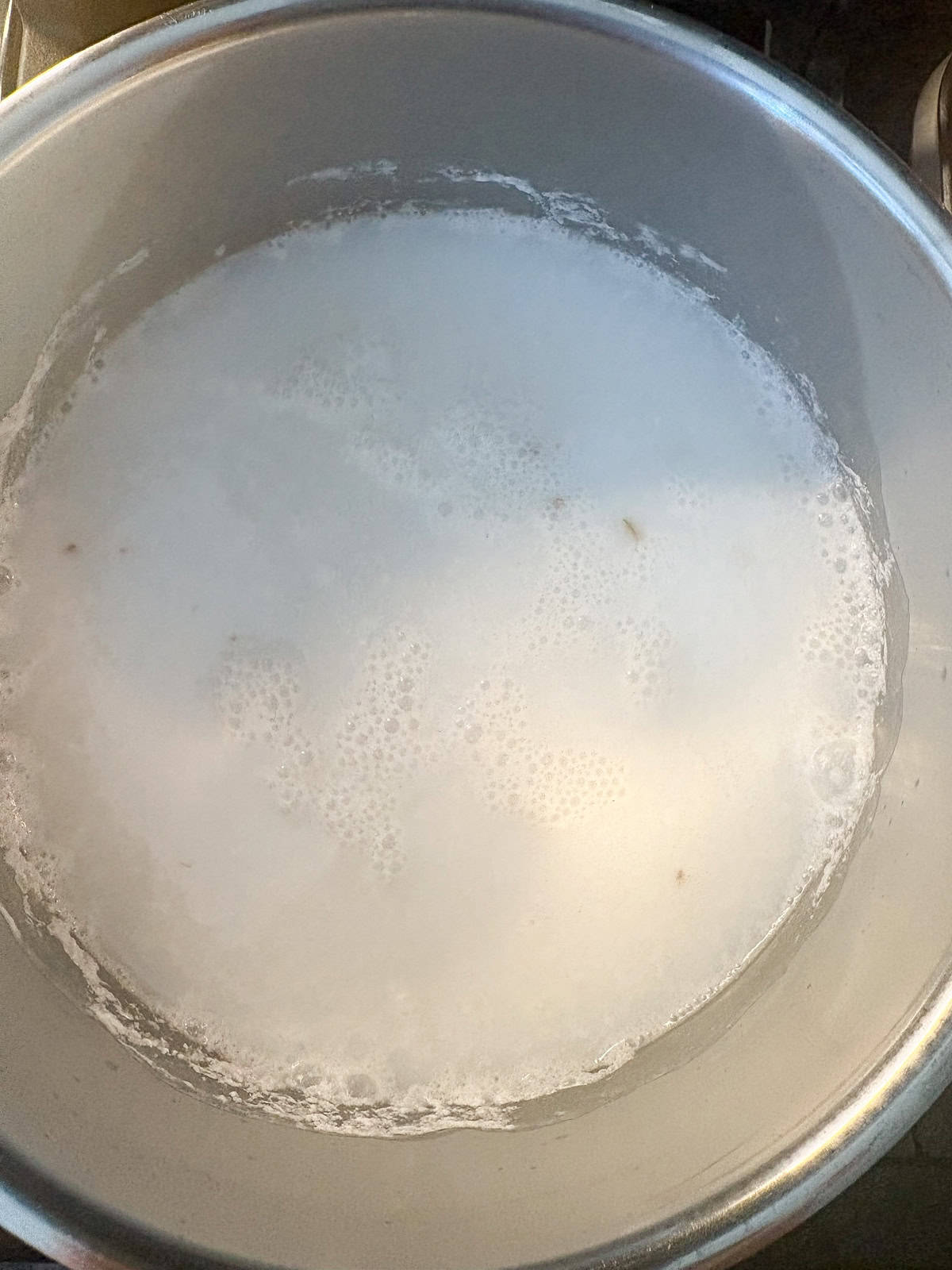 Dry rice added to simmering liquid in a pot.