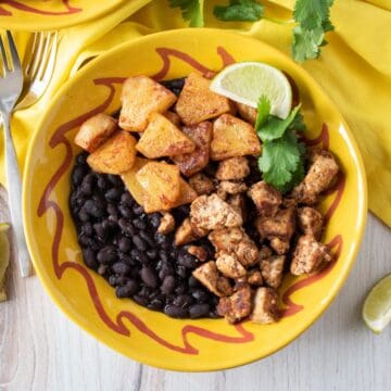 Bowl with jerk tofu and pineapple, over black beans, garnished with cilantro and a lime wedge.