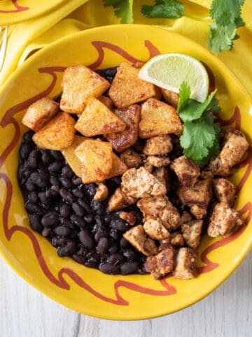 Bowl with jerk tofu and pineapple, over black beans, garnished with cilantro and a lime wedge.
