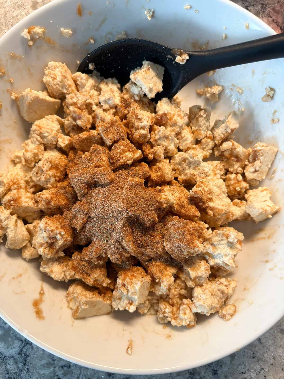 Torn tofu pieces in a bowl, sprinkled with jerk seasoning.