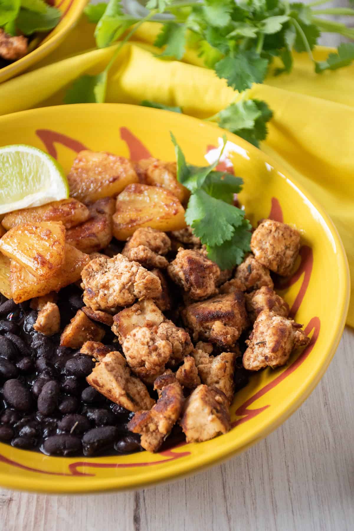Bowl with jerk tofu and pineapple, over black beans, garnished with cilantro and a lime wedge.