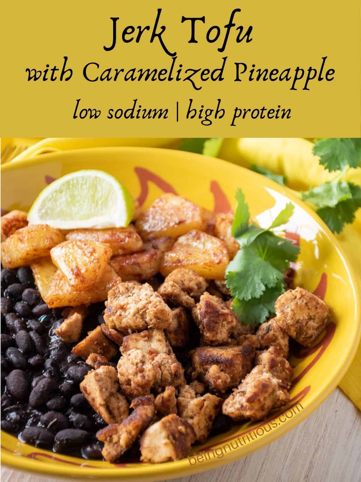 Bowl with tofu and pineapple, over black beans, garnished with cilantro and a lime wedge. Text overlay: Jerk Tofu with Caramelized Pineapple; low sodium, high protein.