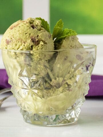 Small glass mug of green colored ice cream with chocolate chips, garnished with fresh mint leaves.