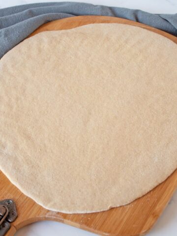 Raw pizza dough, rolled out to a circle, on a pizza peel.