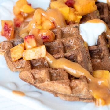 Waffle quarters, arranged on a serving dish, and garnished with chopped fresh peaches, dollops of yogurt, and peach syrup.