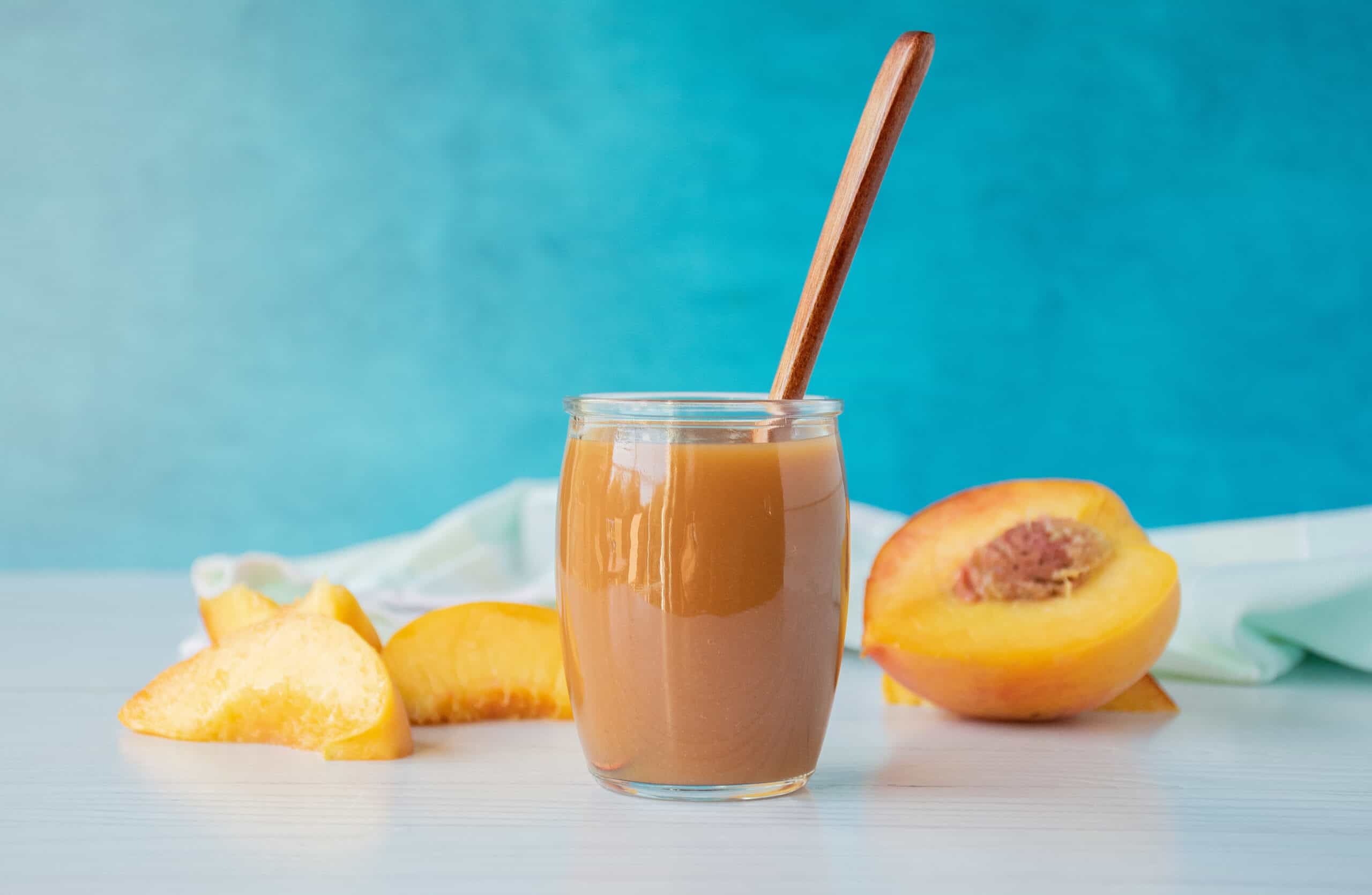 Peach sauce in a small glass jar, with peach slices surrounding.