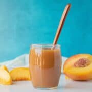 Peach syrup in a small glass jar, with peach slices surrounding.