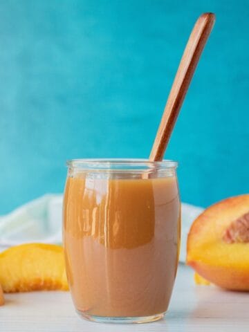 Peach syrup in a small glass jar, with peach slices surrounding.