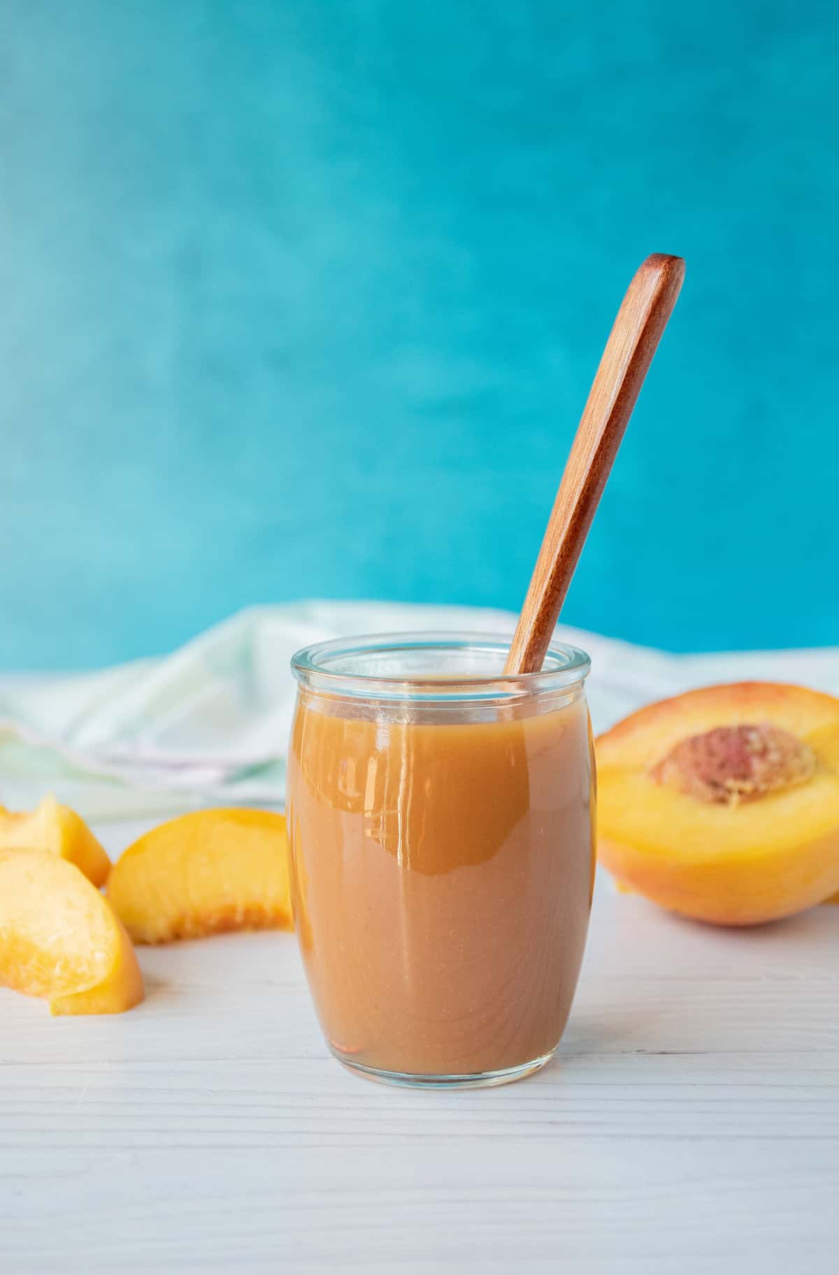 Peach syrup in a small glass jar, with peach slices surrounding.