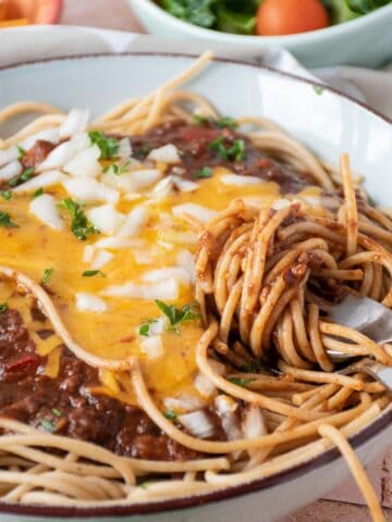 Bowl with spaghetti topped with Cincinnati chili, cheese, and onions, and noodles twirled around a fork.