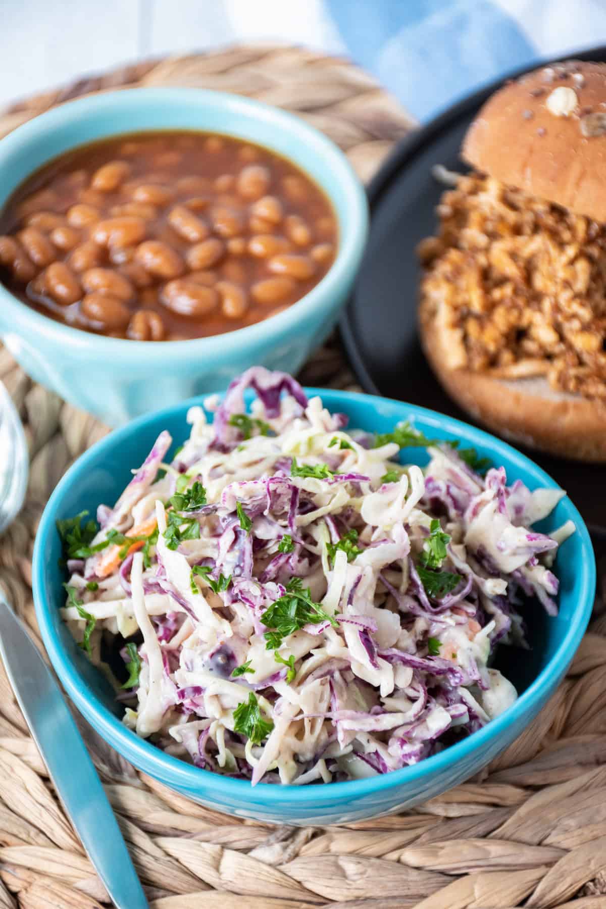 Small bowl of coleslaw, with a BBQ sandwich and baked beans in the background.