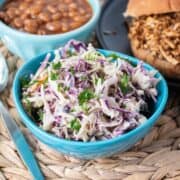 Small bowl of coleslaw, with a BBQ sandwich and baked beans in the background.