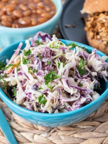 Small bowl of coleslaw, with a BBQ sandwich and baked beans in the background.