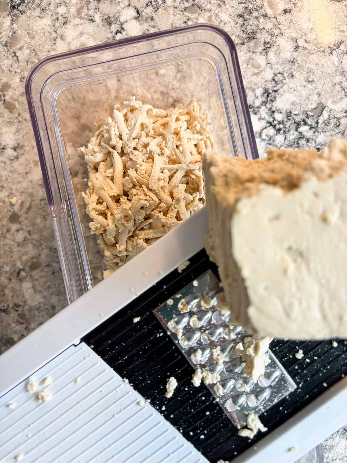 A photo showing how to shred tofu using the large holes on a cheese shredder.