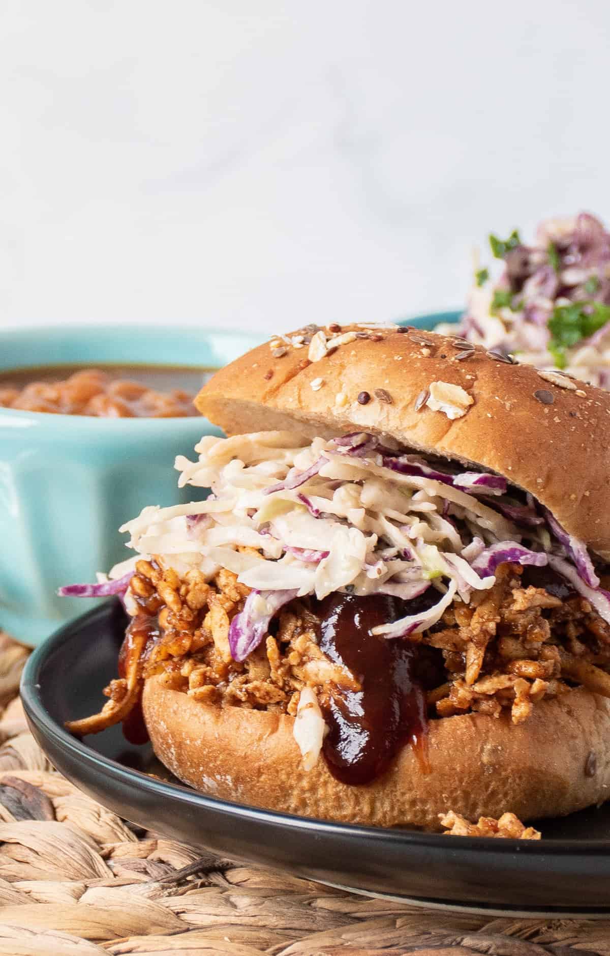 Close up of shredded BBQ tofu sandwich with coleslaw, on a hamburger bun.