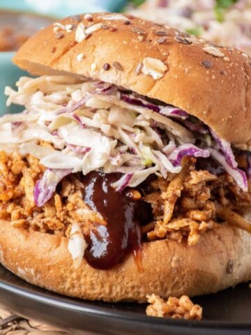 Close up of shredded BBQ tofu sandwich with coleslaw, on a hamburger bun.