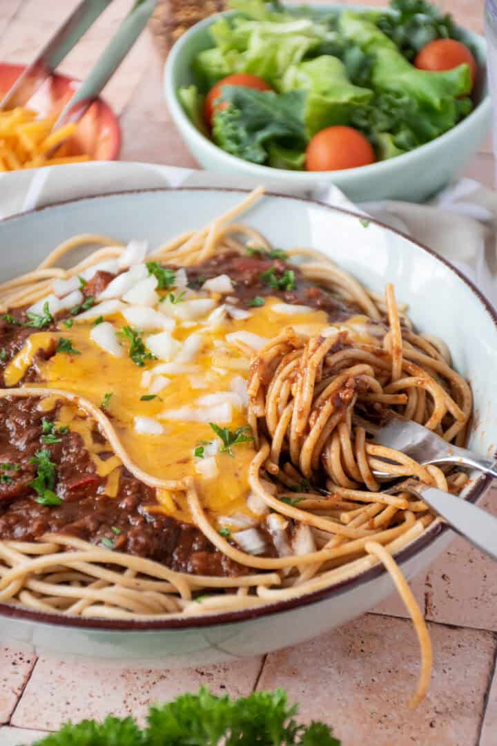 Bowl with spaghetti topped with Cincinnati chili, cheese, and onions, and noodles twirled around a fork.
