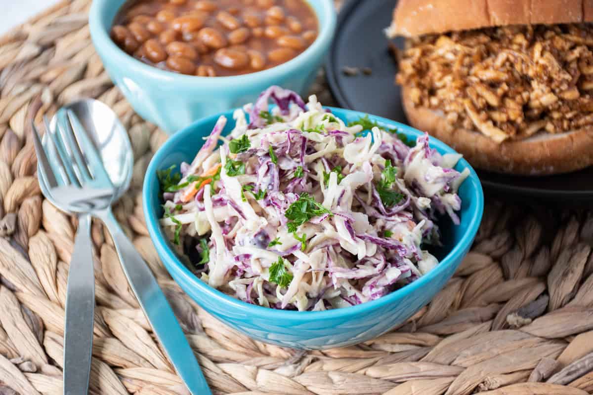 Small bowl of coleslaw, with a BBQ sandwich and baked beans in the background.