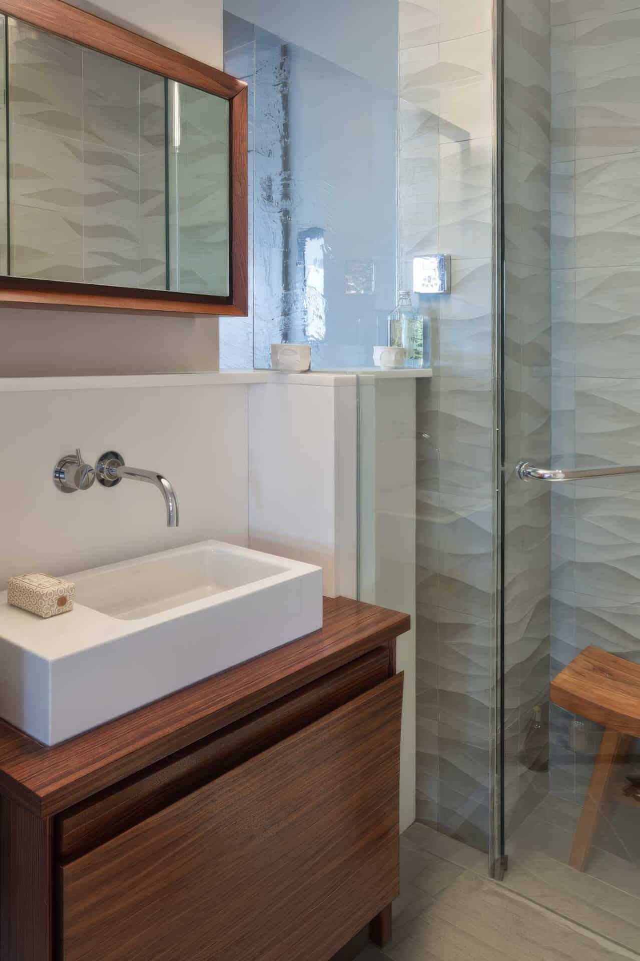 Modern bathroom with textured wall tiles and wooden vanity.