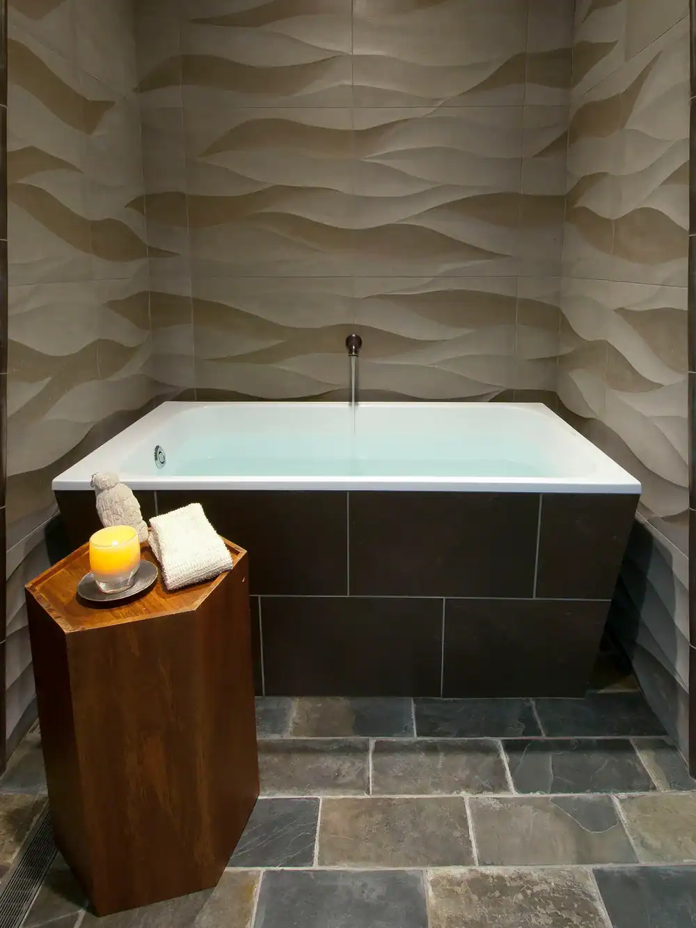 Modern bathtub with textured wall tiles in a stylish bathroom setting.