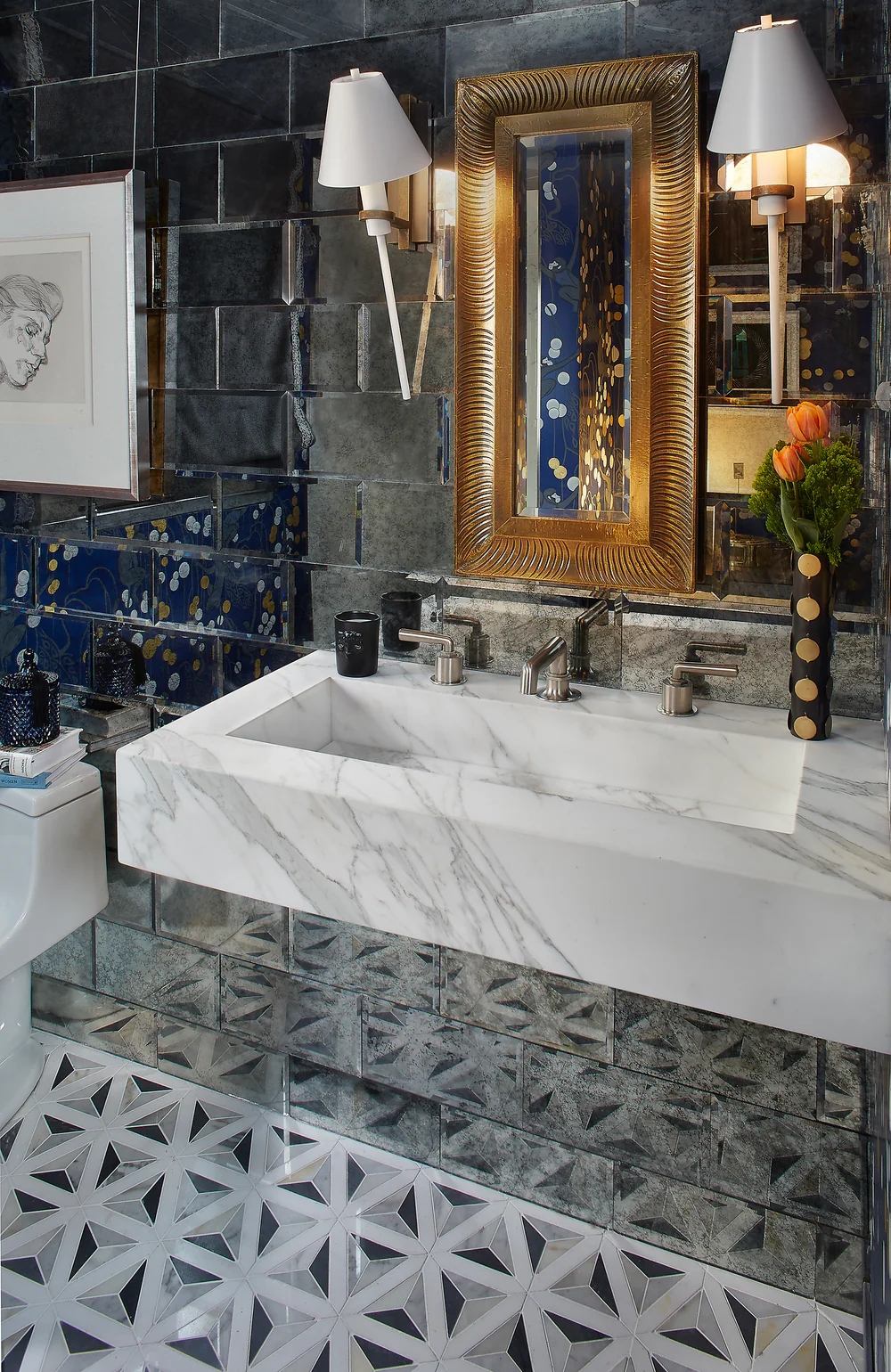 Modern bathroom with marble sink, gold mirror, and black tiled wall.