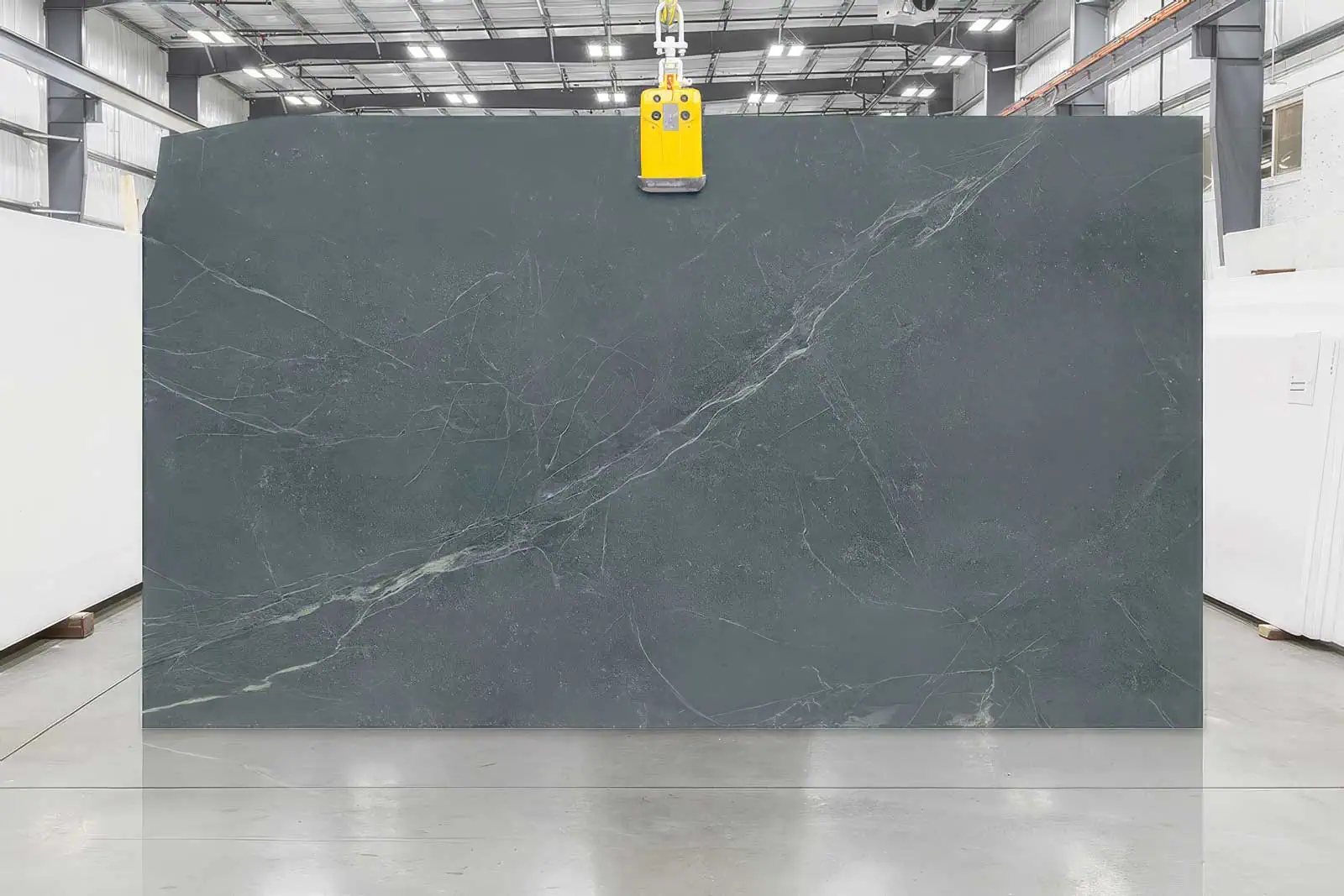 Large dark gray marble slab with white veining in a warehouse setting.