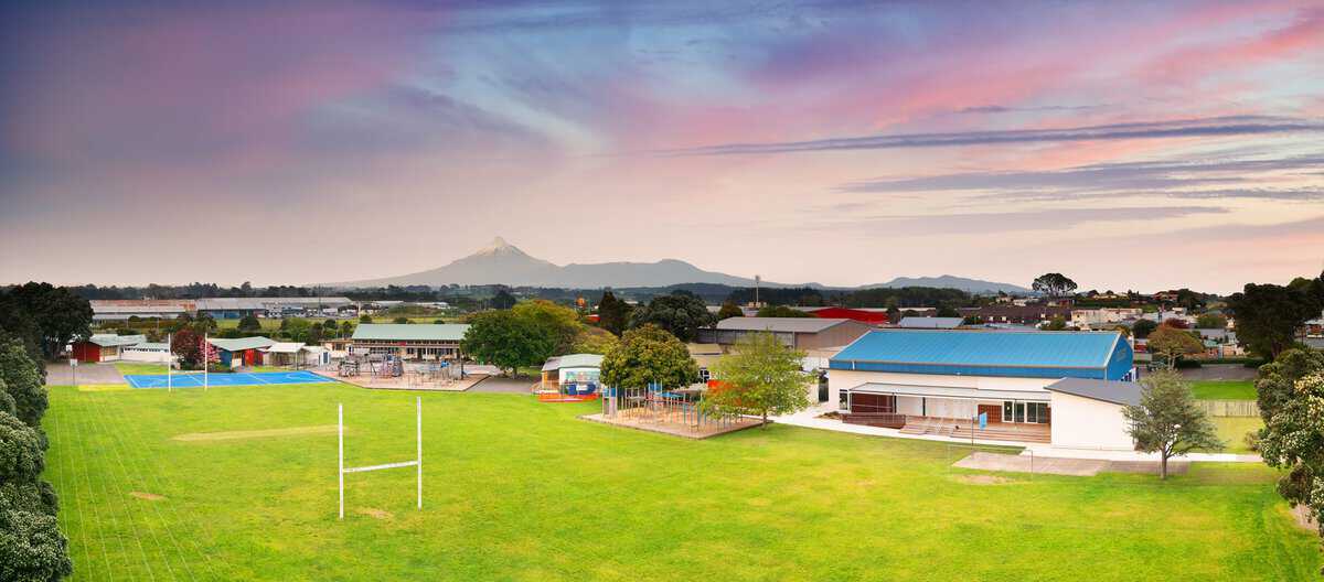 bbksch_Panorama-2_3000px Bright daytime view of Bell Block School with sports fields, playgrounds, and facilities, set against a scenic mountain backdrop.