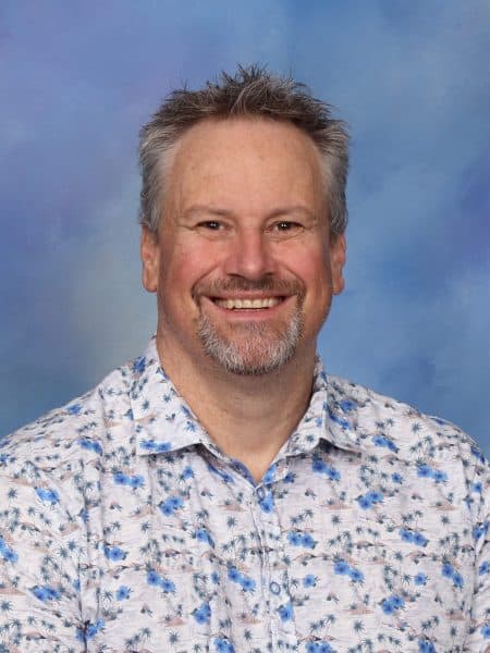 Bright smiling man in front of blue sky background, casual floral shirt, friendly face, professional portrait.