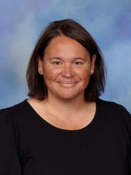 Profile of a female teacher at Bell Block School in New Zealand, smiling and wearing a black top, with a blue sky background, highlighting education professionalism.