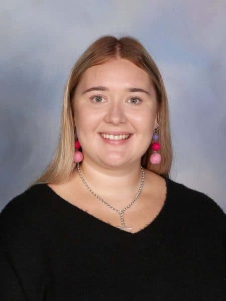 Bright smiling woman with long blonde hair and colorful pom-pom earrings, wearing a black top, portrait for Bell Block School.