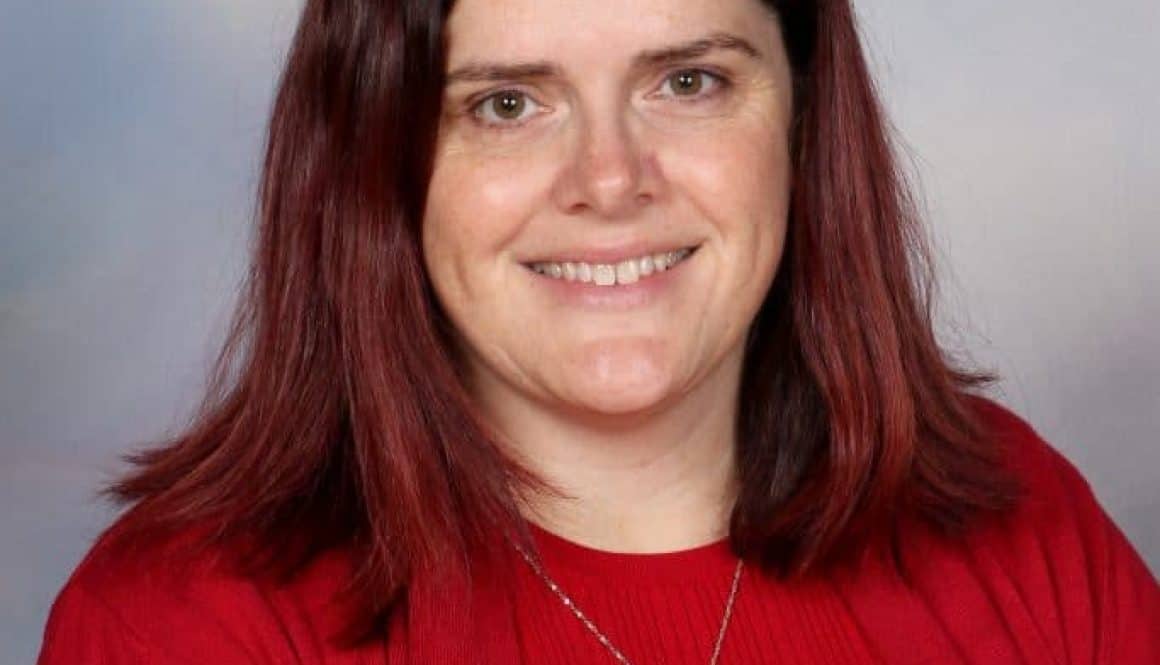 Dedicated female teacher at Bell Block School, New Zealand, smiling in red attire.
