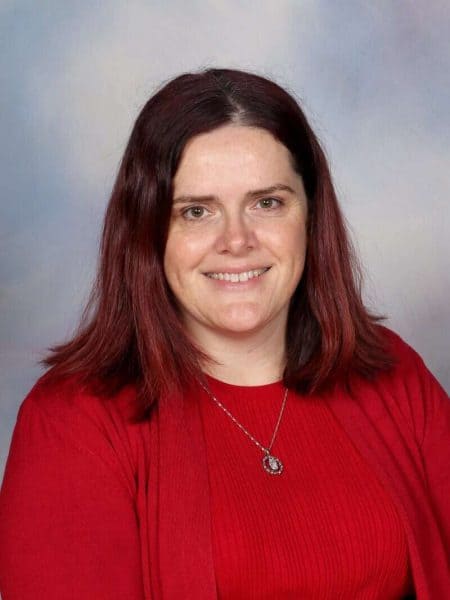 Dedicated female teacher at Bell Block School, New Zealand, smiling in red attire.