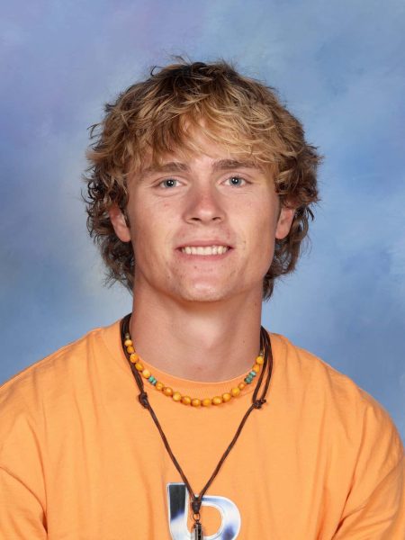 Student Monty Mills smiling in school portrait, wearing an orange shirt and beaded necklace.