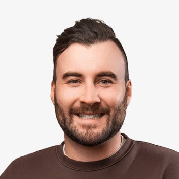 Smiling man with a beard and casual clothing, facing forward in a studio portrait.