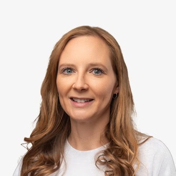 Portrait of a smiling woman with long, wavy hair and blue eyes, wearing a white top.