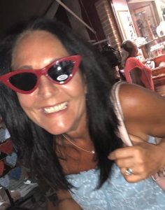 Woman with black hair and red sunglasses smiling in a cafe.
