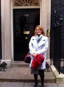 Smiling woman standing outside a building entrance, holding a red bouquet, in front of a black door.