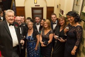 Group of staff members at a formal event, smiling and holding drinks, in an elegant indoor setting.