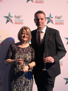 Two professionals, a woman and a man, at an awards ceremony holding glasses of wine.
