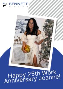 Woman in white dress holding a gift beside a Christmas tree, celebrating work anniversary.