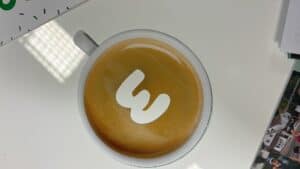 Coffee cup with Bennett Staff logo, on a white table, with a blurred background.